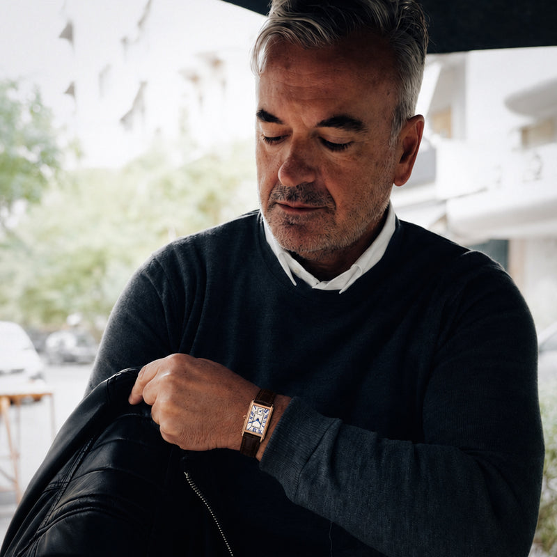 A distinguished man wearing the 1927 gold tank watch with brown leather strap at an outdoor cafe
